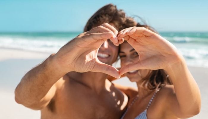 Couple making a heart shape on the beach, representing summer romance and real connection